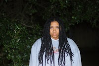 a woman with long dreadlocks standing in front of a tree