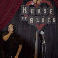 a man holding a microphone in front of a house of blues sign